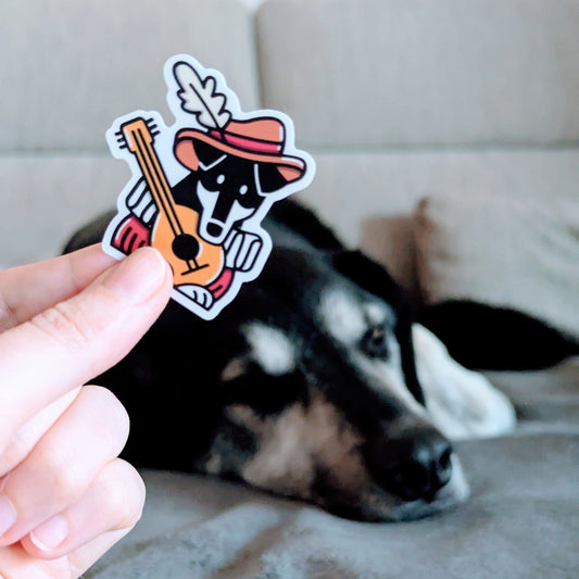 Ein Hund-Barde-Sticker hochgehalten neben einem echten Hund.